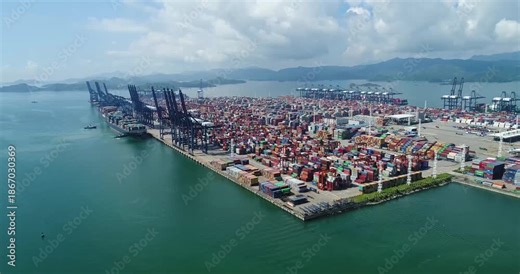 This dynamic video captures the bustling operations of a large-scale logistics port and shipping terminal, featuring massive container ships loading and unloading cargo, towering port cranes moving co