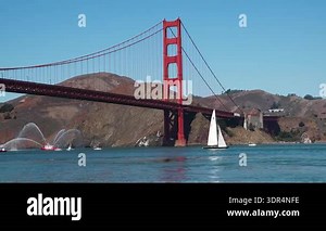 Boats navigate the waters near the Golden Gate Bridge in San Francisco. The sun shines brightly on the bridge and surrounding hills. People enjoy the sight of this famous landmark.