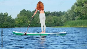 Woman paddleboarder transforms lake in aquatic playground. Young woman elevates overall enjoyment of water-centric pastimes